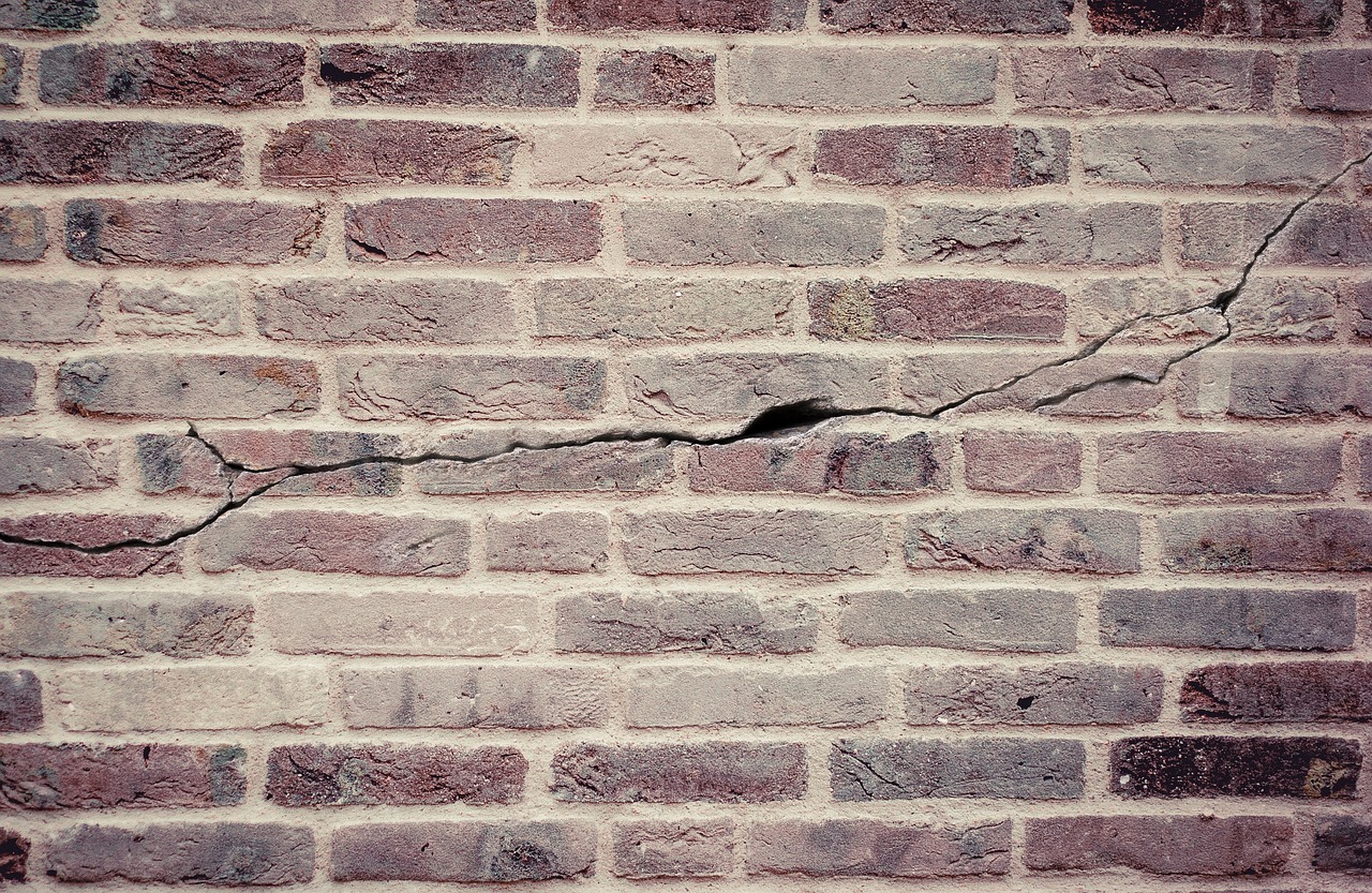 Immagine che mostra un muro con crepe, strumenti fai da te e materiali per la riparazione.