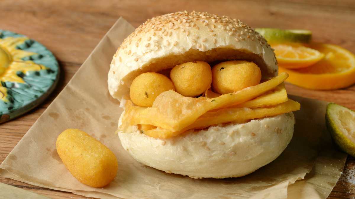 Varietà di street food siciliano, con arancini, pane con la milza e cannoli su un mercato.